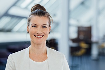 Susanne Grund, dunkelbraune Haare zu einem Dutt gebunden, schwarze Ohrstecker, lächelnd, weißer Blazer