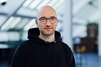 Jan Hößler, schwarzer Kapuzenpullover, Brille, lächelnd