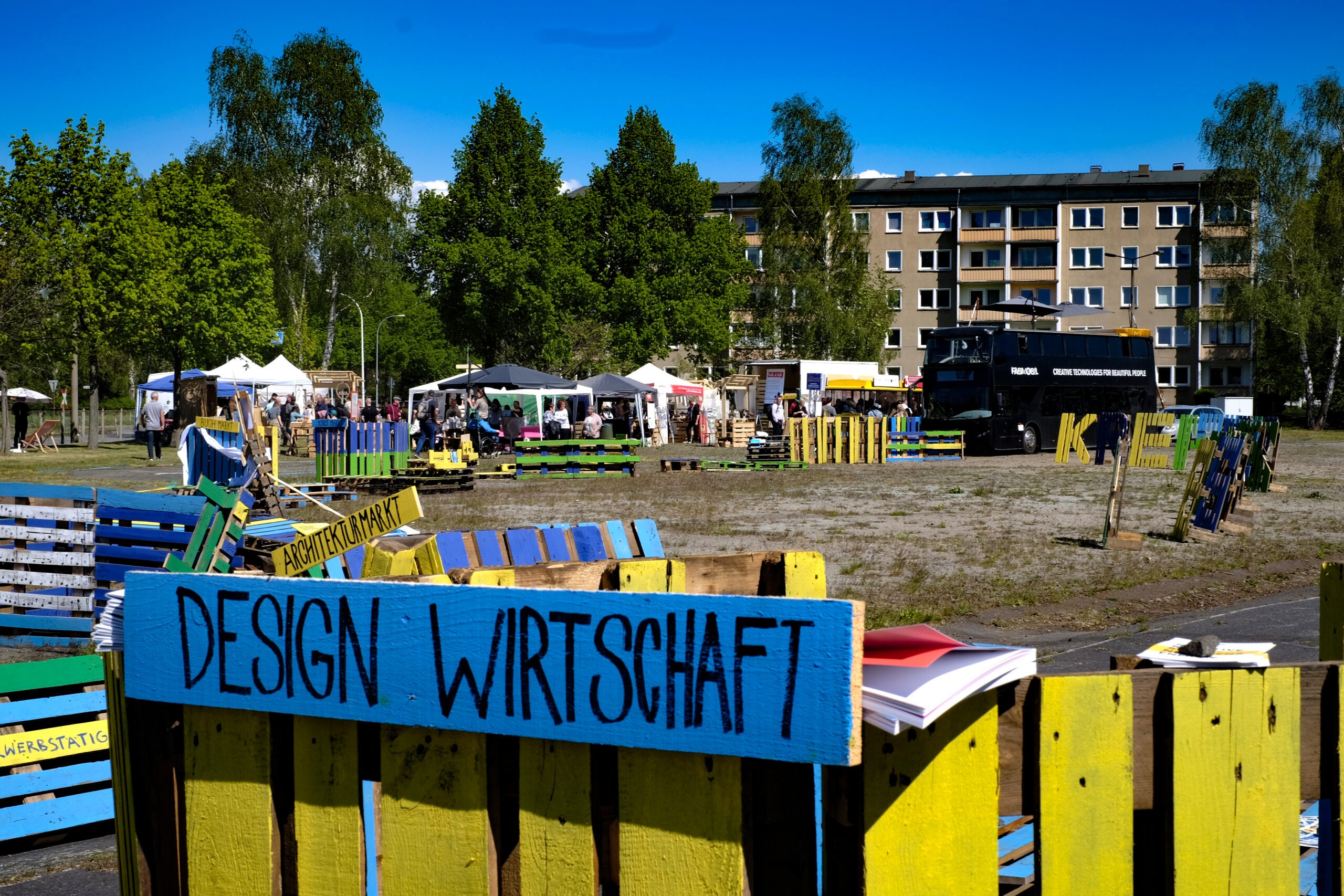 das Wort Design Wirtschaft in schwarz auf blauem Hintergrund auf einem Stück Holz im Hintergrund Bäume und ein Haus