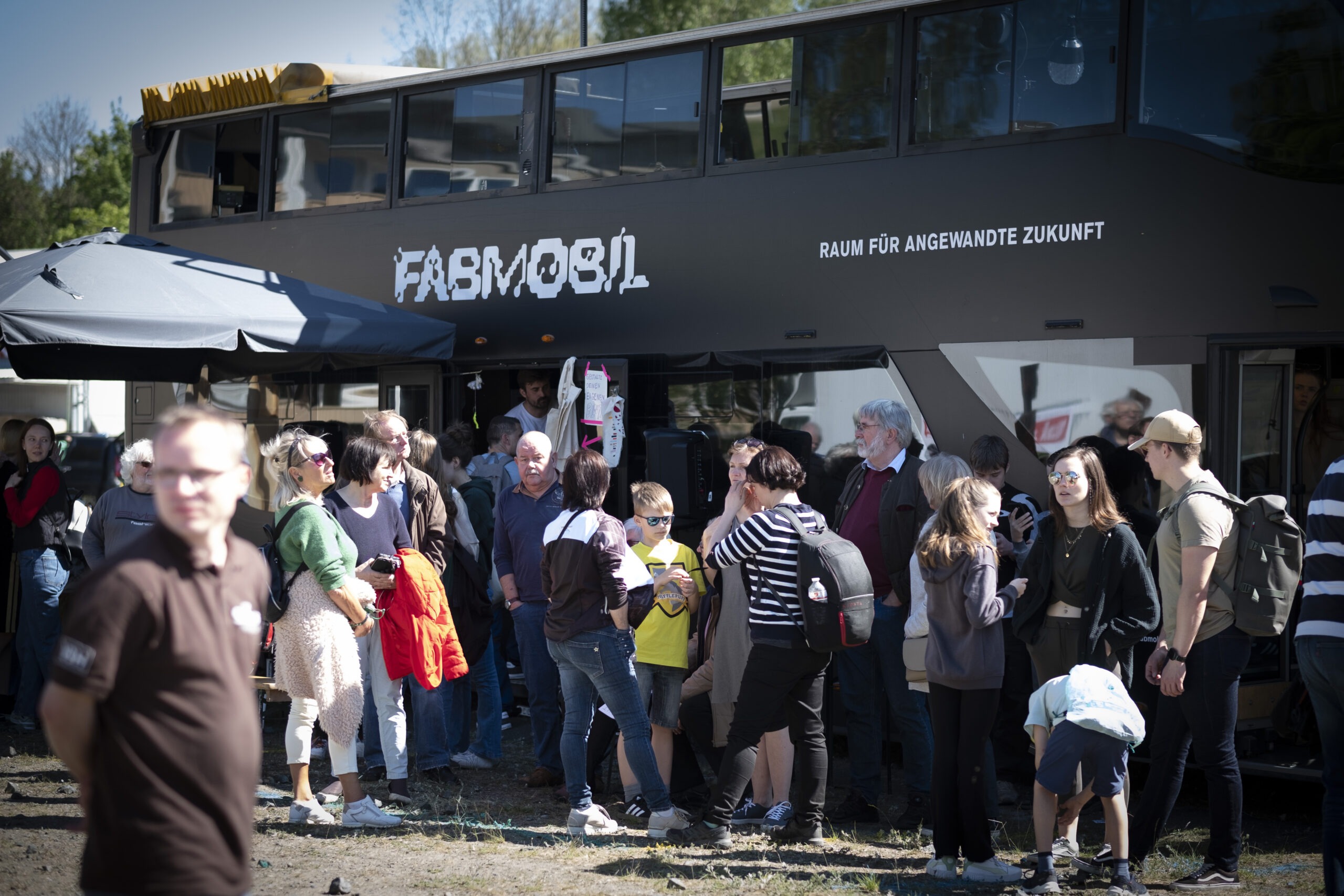 der schwarze Bus des Fabmobils im Vordergrund eine Gruppe Menschen