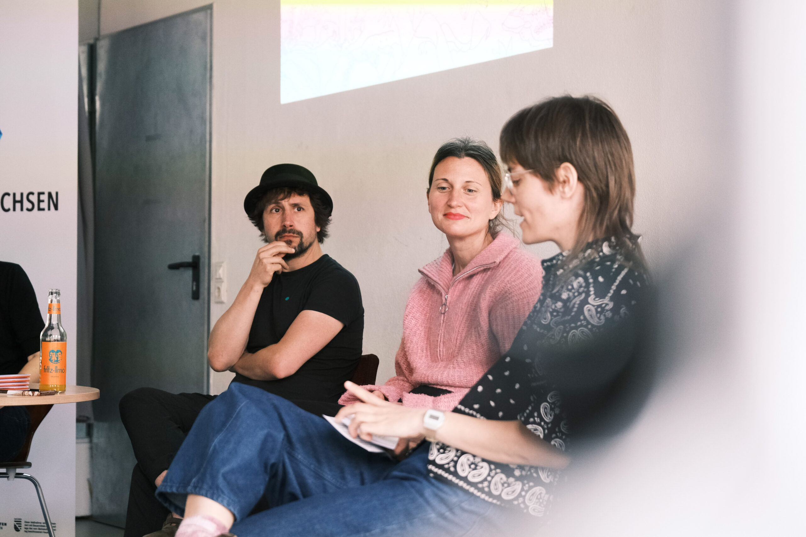Mann mit Hut neben zwei Frauen die gemeinsam diskutieren