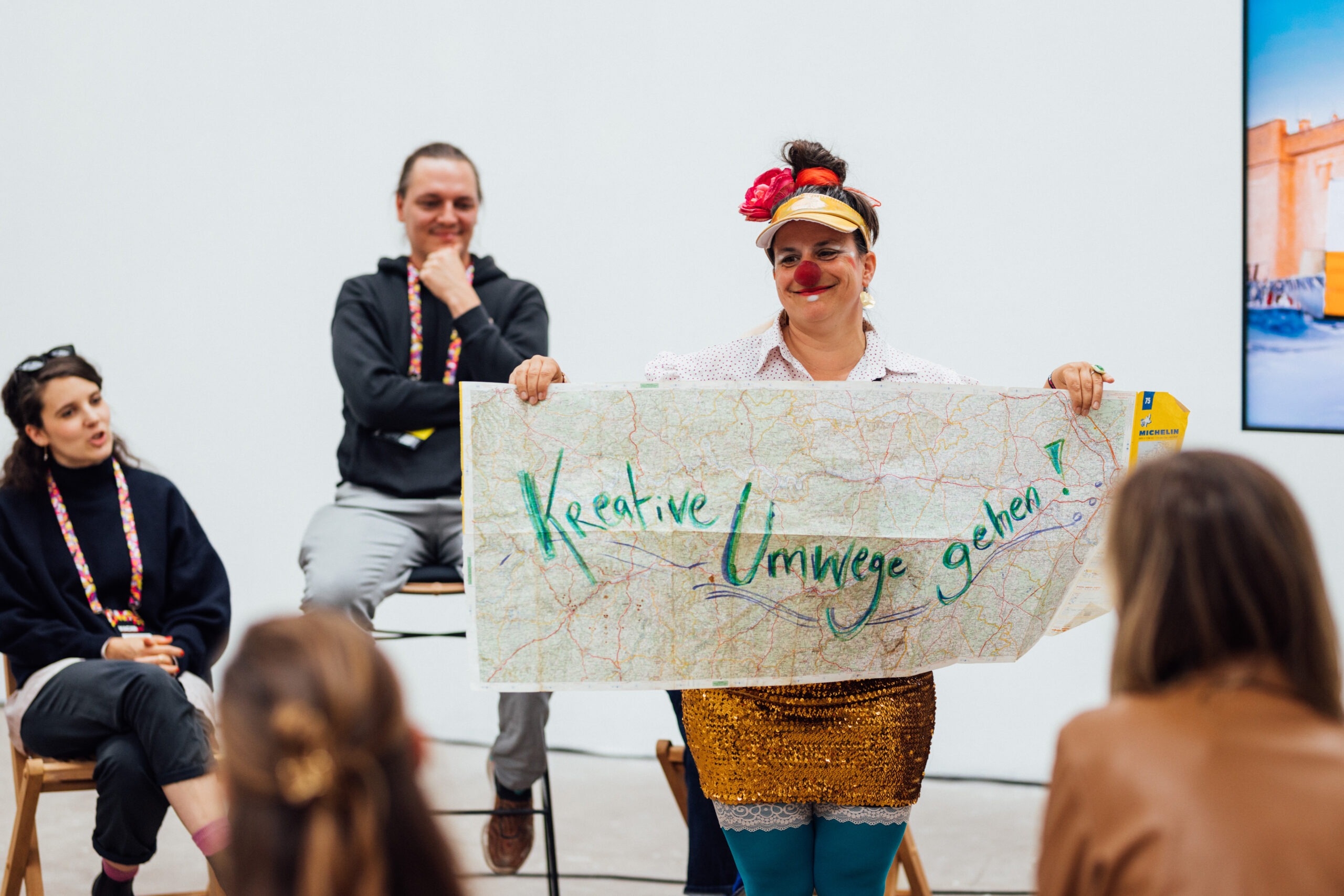 Eine Frau mit Clownsnase hält ein Banner mit der Aufschrift Kreative Umwege gehen