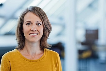 Frau mit dunkelblonden schulterlangen Haaren und gelbem Shirt lächelt in die Kamera