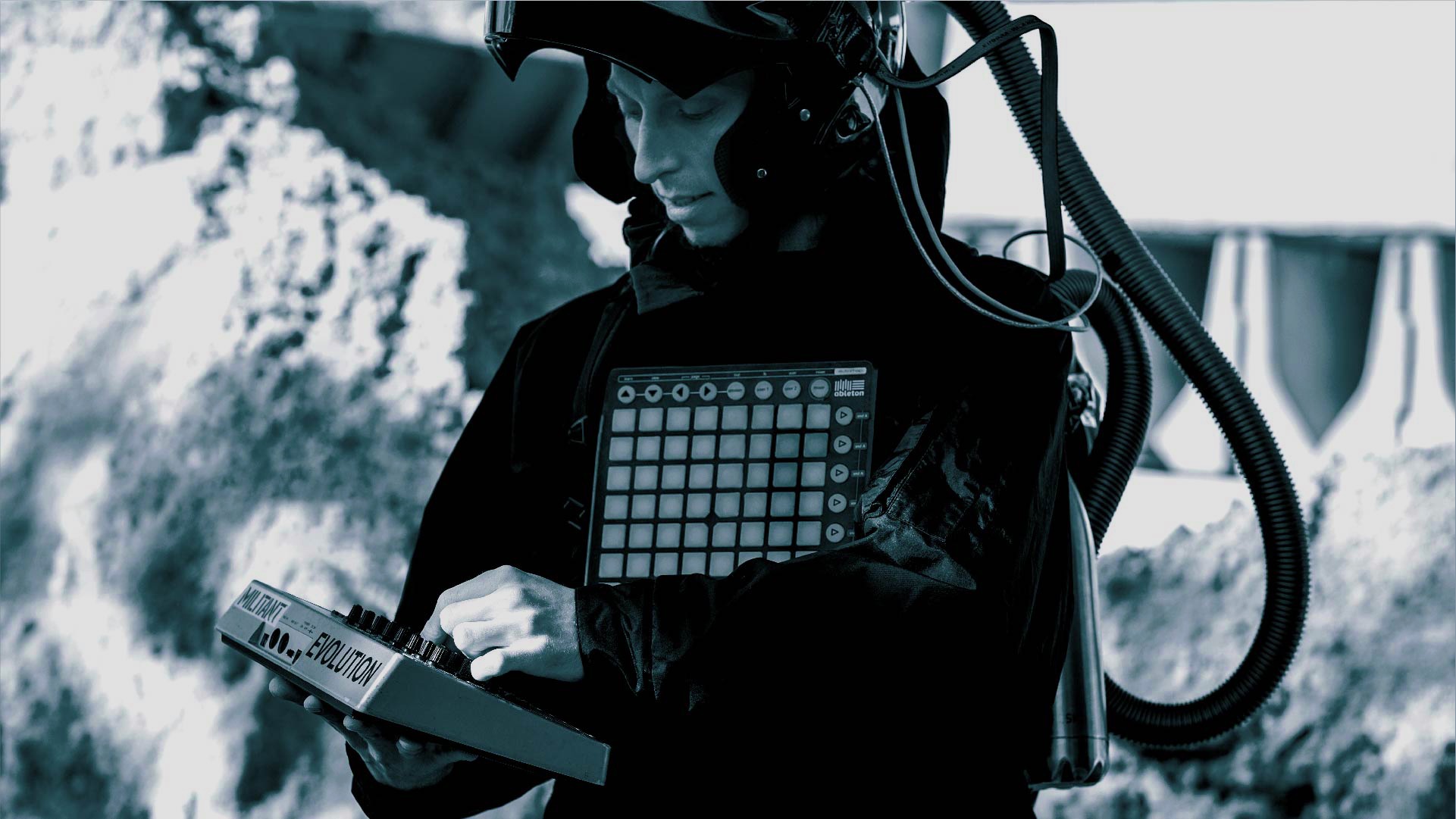 Ein schwarz-weißes Bild. Zu sehen ist ein weißer Mann mit einem Synthesizer in der Hand und einem Helm mit Schlauch auf dem Kopf