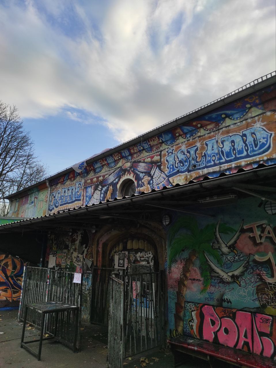 Die Fassade des Clubs Conne Island mit vielen Graffittis, im Hintergrund blauer Himmel und weiße Wolken.