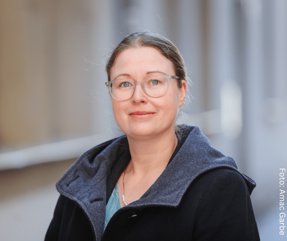 Weiße Frau mit Brille und zusammengebundenen haaren, sie trägt eine dunkleJacke