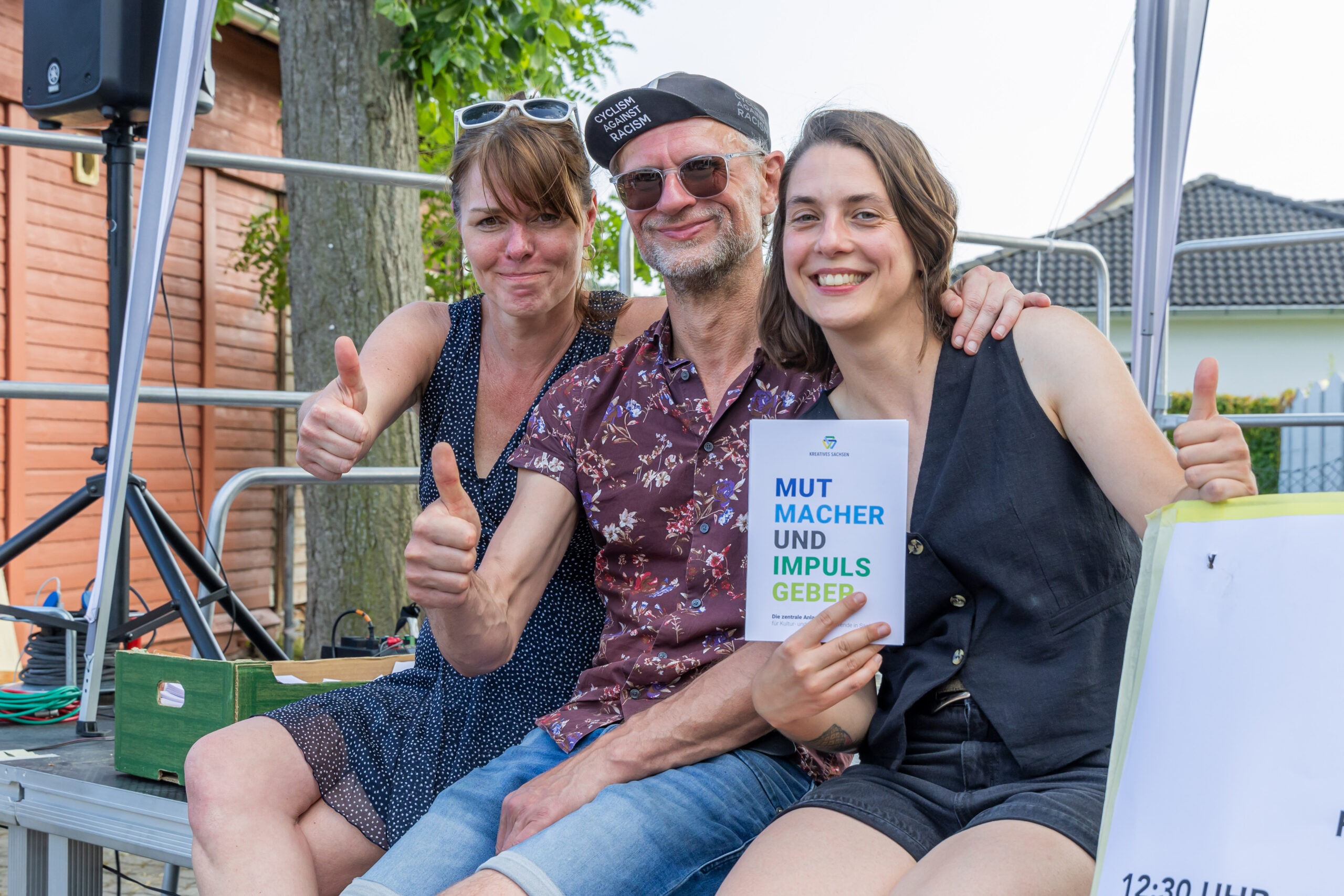 Ein Mann und zwei Frauen halten den Daumen hoch, in ihren Händen eine Broschüre mit der Aufschrift Mutmacher und Impulsgeber