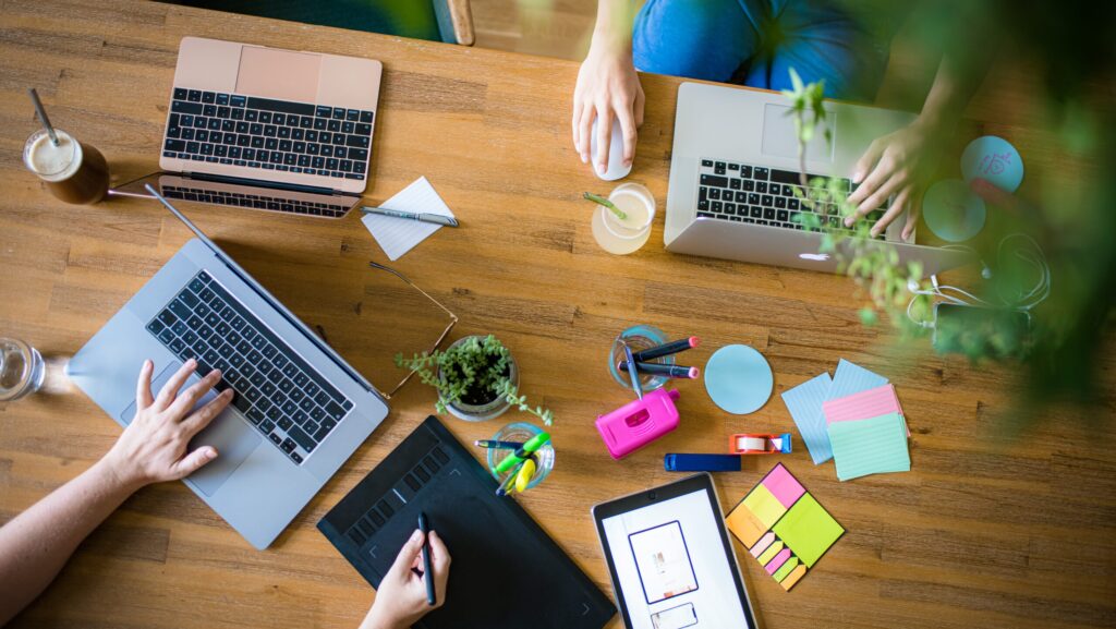 Tisch von oben mit aufgeklappten Laptops, Stiften und Klebezetteln